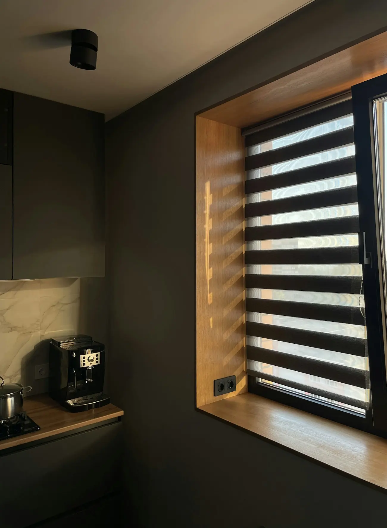 Zebra perde uygulaması: koyu tonlu bir mutfakta ışığı bantlar hâlinde geçiren gün ve gece perdesi